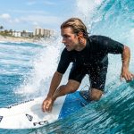 Surfer wearing protective ear plugs catching a sunny Florida wave.