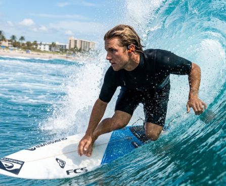 Surfer wearing protective ear plugs catching a sunny Florida wave.